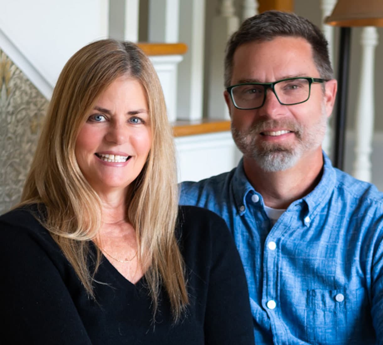 A smiling woman and man pose together in a home setting.