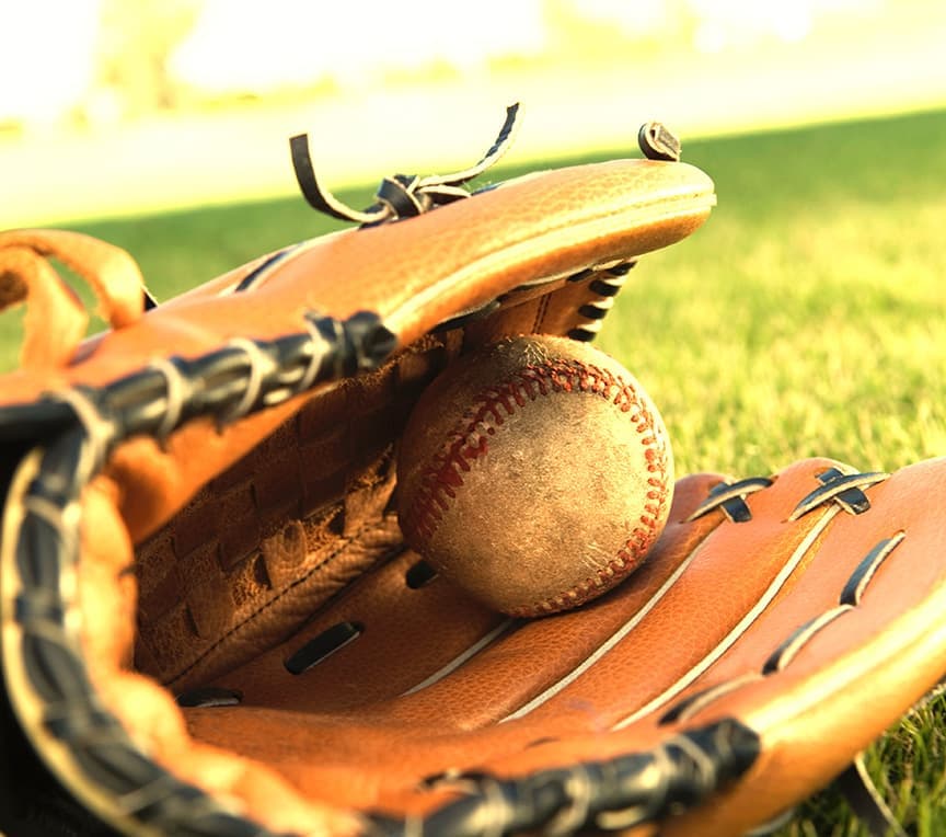 A baseball nestled inside a leather glove on grass.