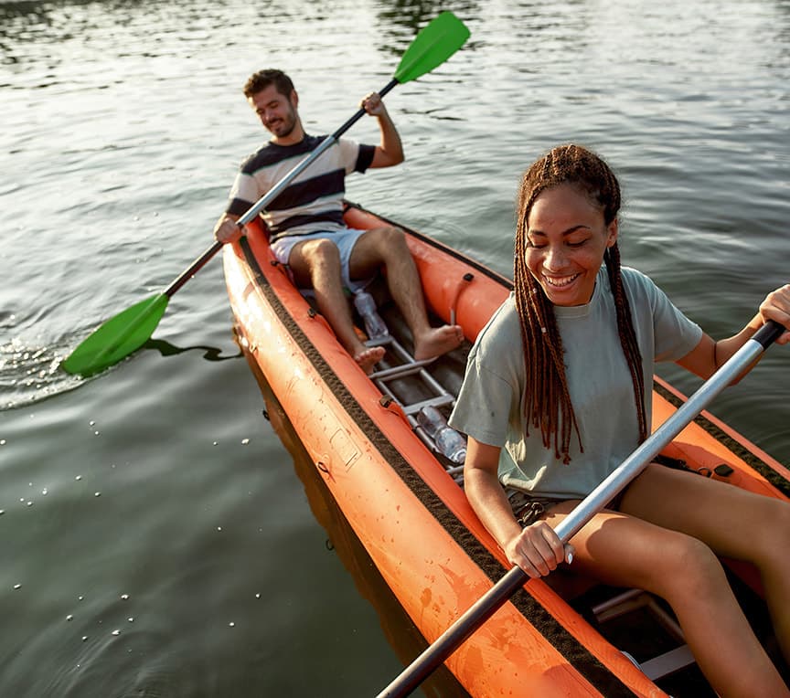 A man and woman happily kayak together on a calm lake.