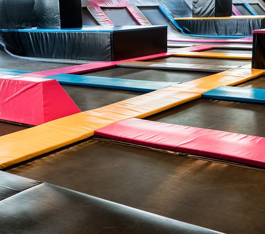A vibrant indoor trampoline park with various colorful trampolines and soft mats.