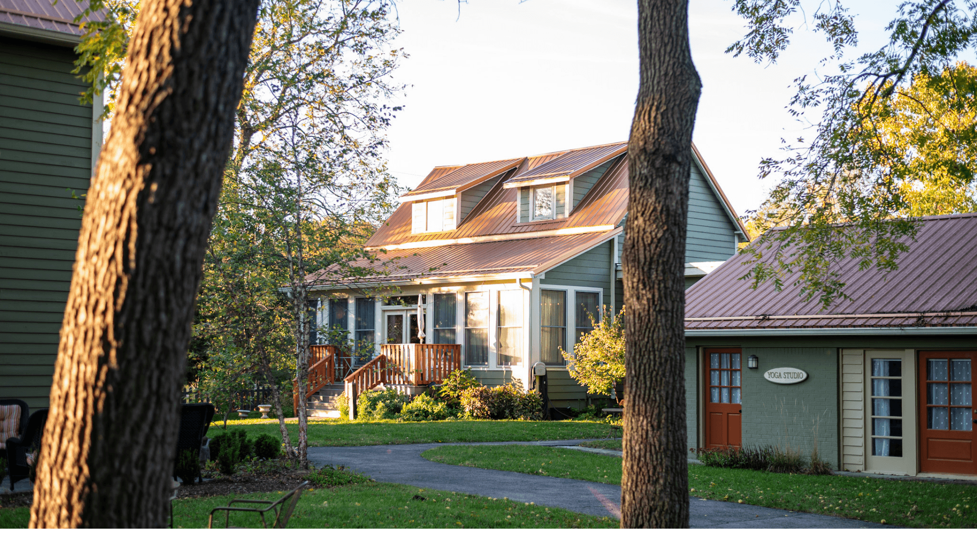 A quaint multi-story house with a red metal roof surrounded by trees and a well-kept lawn.