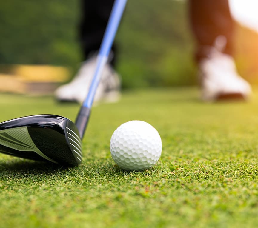 A golf club is poised above a white ball on a green golf course.