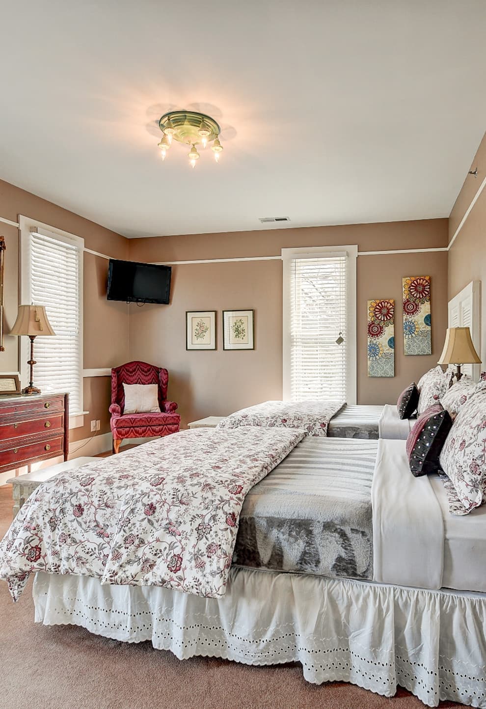 A cozy bedroom featuring two twin beds, a red armchair, and decorative wall art.