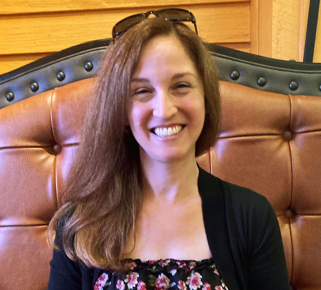 A smiling woman with long hair sits against a leather upholstered backdrop.